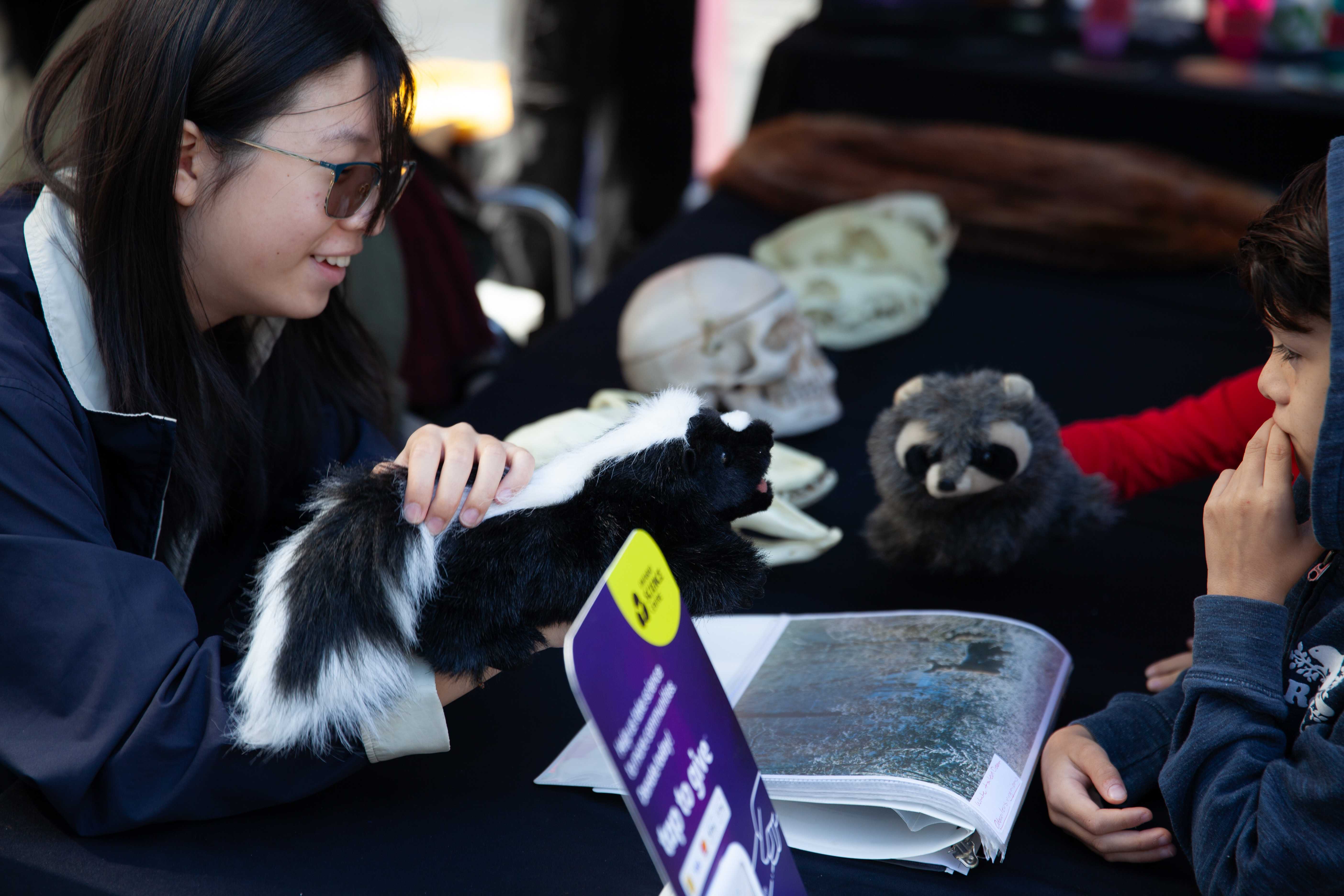 Un groupe autour d'une table où on voit des crânes en arrière plan jouent avec deux marionnettes d'animaux en peluche.