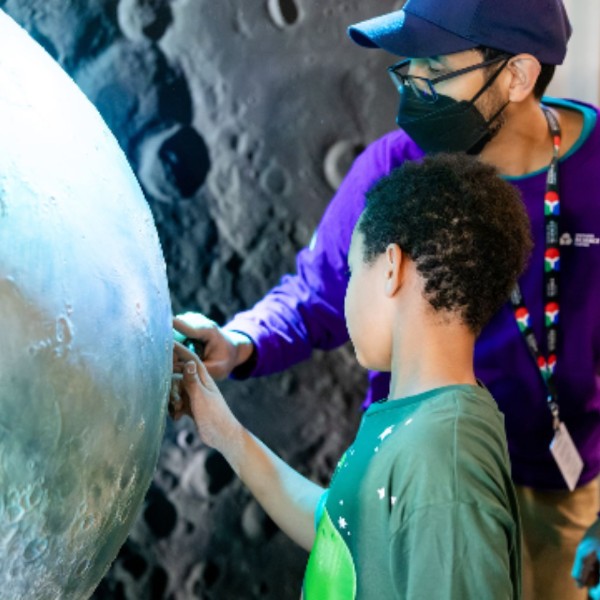 Un membre du personnel d'un centre des sciences et un garçon regardent une exposition sur la Lune.