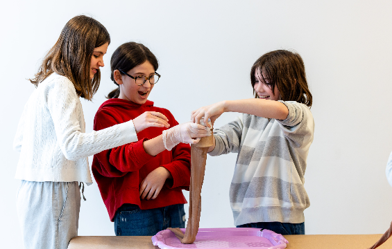[A group of three kids playing with clay and slime.][Un groupe de trois enfants jouant avec de l'argile et de la pâte à modeler.]