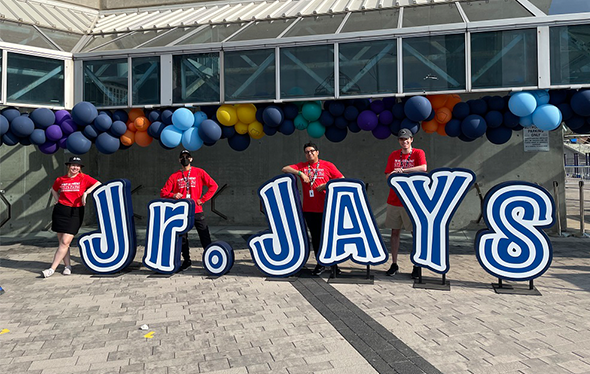 Quatre employés du Centre des sciences debout à côté d'un enseigne Jr. Jays géant