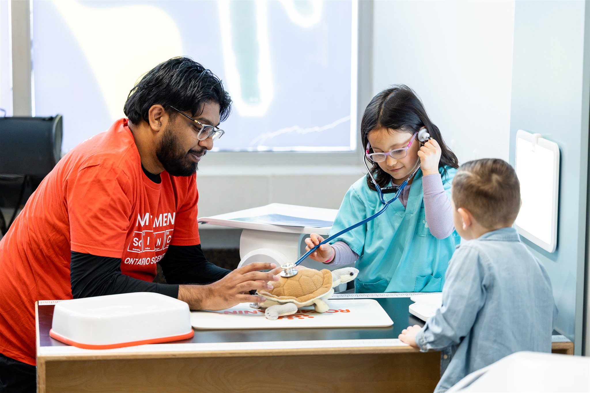[Kids and Scientist examining a turtle toy with stethoscope.][Des enfants et un scientifique examinent une tortue-jouet avec un stéthoscope.]