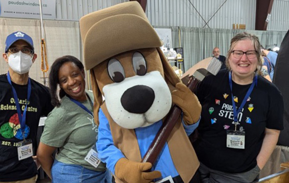 Trois employés du Centre des sciences posent avec la mascote de l'exposition Rockhound Gemboree.
