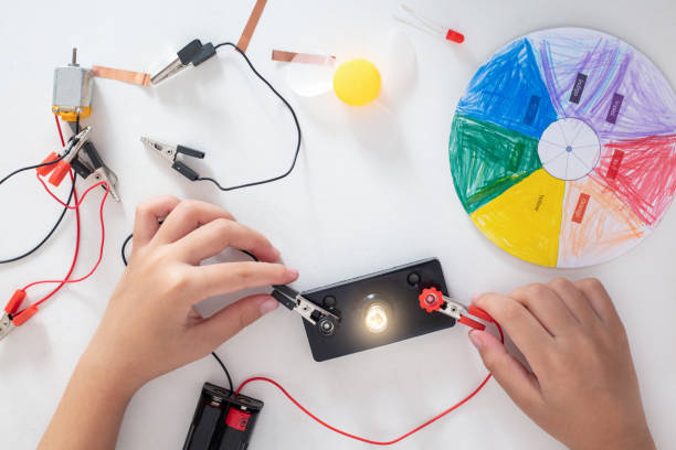 Des mains d'enfant manipulent un circuit électrique qui allume une ampoule.