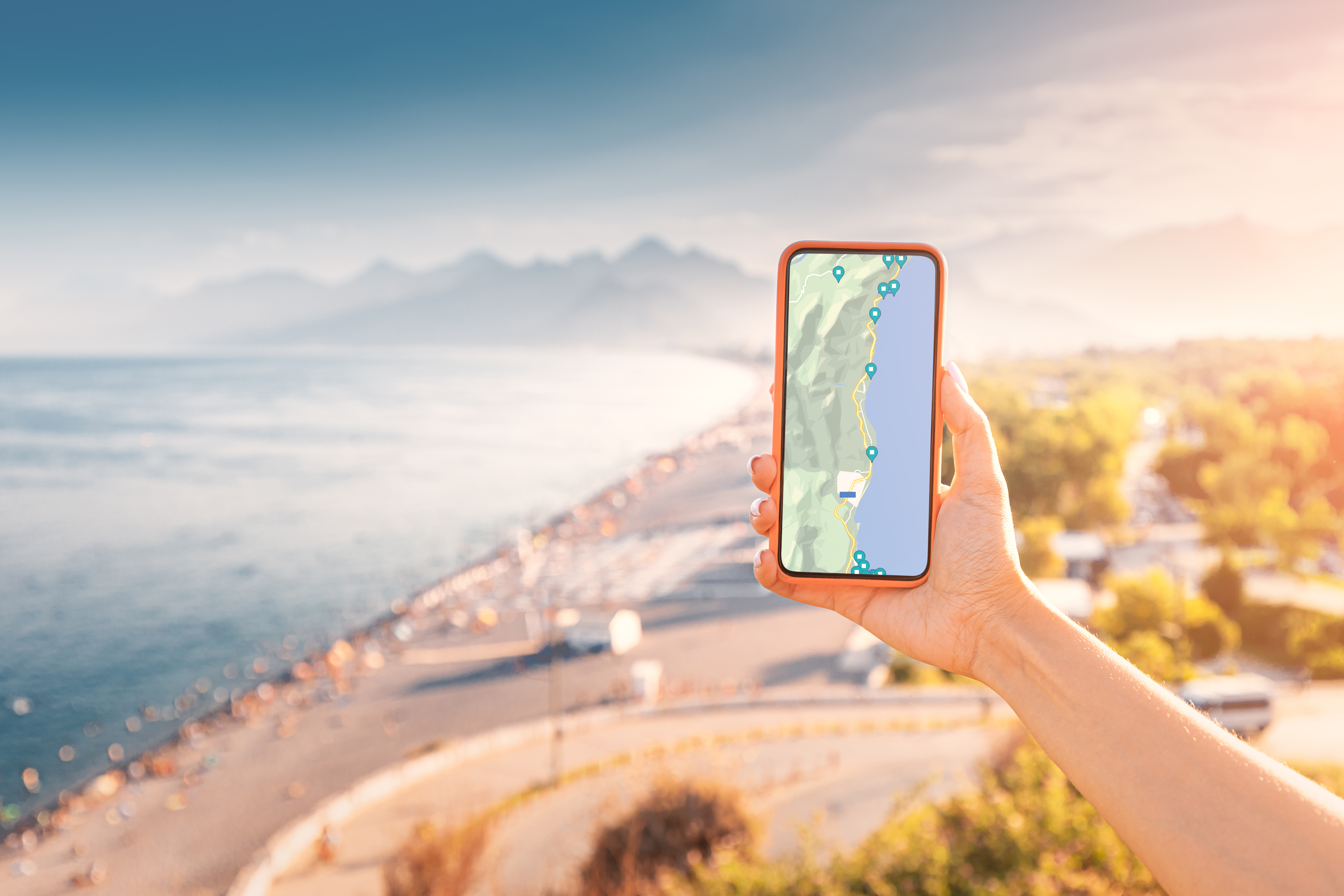 Une main tient un téléphone intelligent affichant des repères sur le paysage à l'arrière plan.