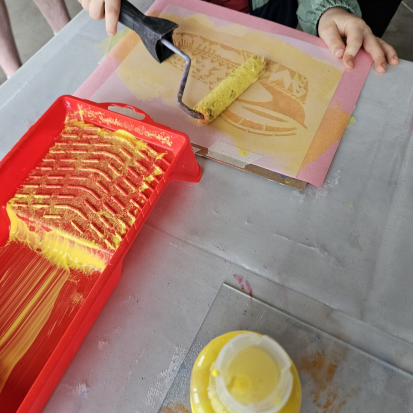 Une main d'enfant applique un rouleau de peinture jaune sur un pochoir. // A child's hand applies a roll of yellow paint on a stencil.