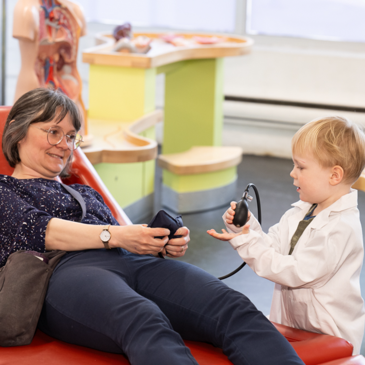 Un garçon portant une blouse de médecin vérifie la tension artérielle de sa grand-mère au lit.