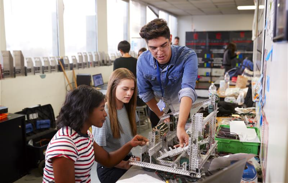 Un professeur et deux élèves construisent une machine en cours de sciences.