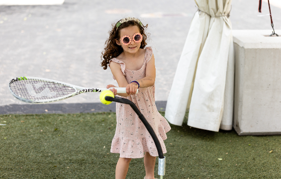 Une petite fille qui joue au tennis avec une raquette et une balle.