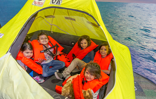 Cinq enfants portant des gilets de sauvetage partagent un radeau de sauvetage.