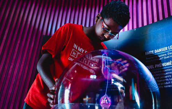Un jeune garçon pose sa main sur la boule de verre à plasma et observe l'étincelle électrique qui touche sa paume à l'intérieur de la boule.