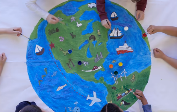 Des enfants peignent un grand globe terrestre sur du papier.