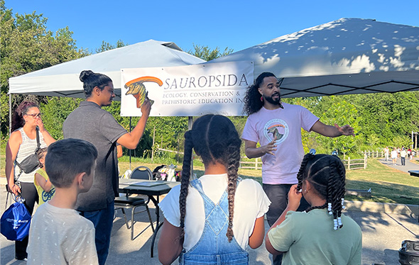 Trois enfants et trois adultes interagissent avec le stand des sauropsides.