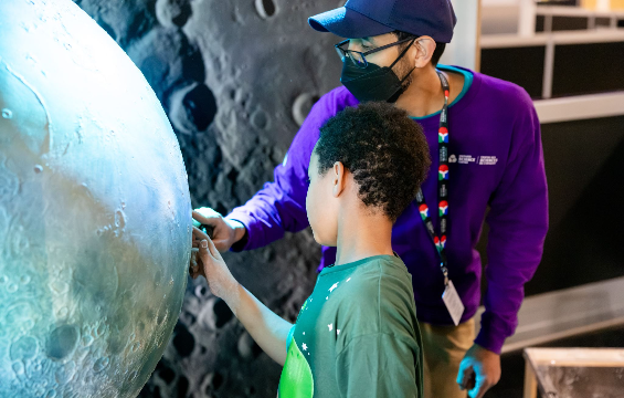 Un membre du personnel d'un centre des sciences et un garçon regardent une exposition sur la Lune.